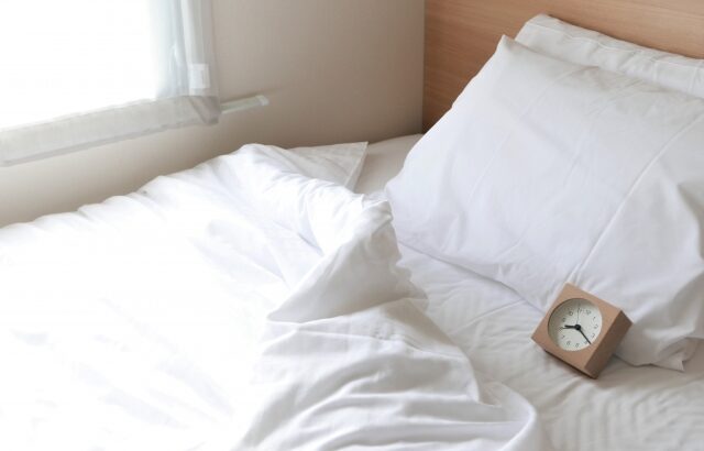 目覚まし時計が置かれたベッドに朝日が差し込む画像