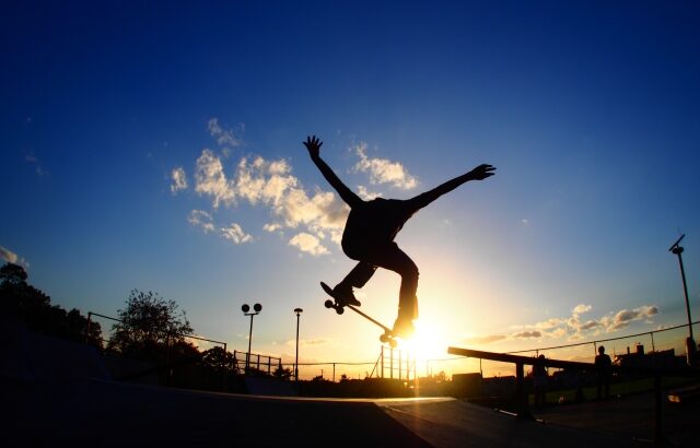 夕日をを背景にスケボーでジャンプしている人の画像